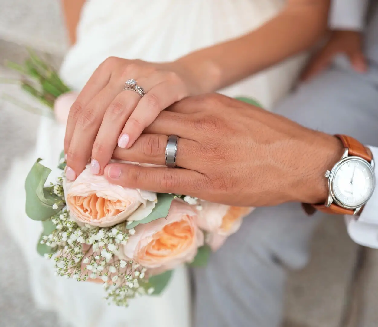 Manos de novios entrelazadas sobre un ramo